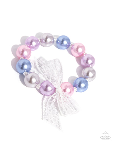 Strung along an elastic stretchy band, a collection of glossy colorful pearls alternate with dainty white pearls along the wrist. An airy, chiffon white ribbon is tied in the center of the pearls for a refined finish.