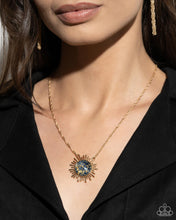 Load image into Gallery viewer, Gliding along a dainty gold chain, a gold sunburst pendant, embellished with gold foil against a navy backdrop creates a stunning sunny statement. Features an adjustable clasp closure. 
