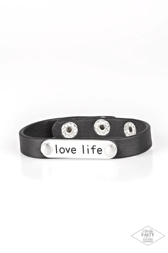 A silver plate engraved with the inspirational phrase “love life” is studded in place along a skinny strip of black leather. Brushed in a shiny finish, the dainty band wraps around the wrist in a simply seasonal style. Features an adjustable snap closure.  Sold as one individual bracelet.  This Fan Favorite is back in the spotlight at the request of our 2019 Life of the Party member with Black Diamond Access, Britney G.