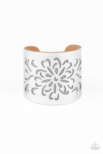 A thick piece of Ash leather peeks out beneath an airy floral pattern stenciled into a thick silver cuff, creating a whimsical display around the wrist.