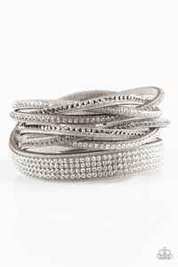 An elongated gray suede band is encrusted in sections of braided white, smoky, and hematite rhinestones and rows of neatly stacked white rhinestones. The elongated band double wraps around the wrist for a fierce one-of-a-kind look. Features an adjustable snap closure.