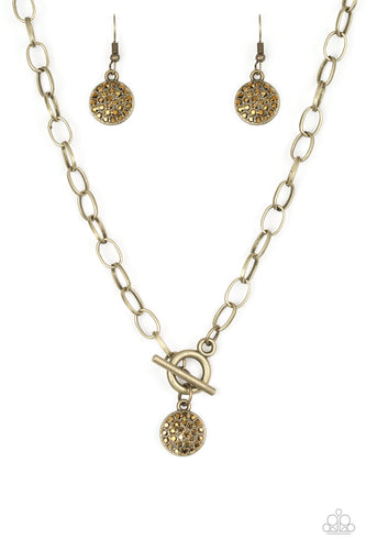 Encrusted in glittery aurum rhinestones, a dainty brass disc swings from the bottom of a glistening brass chain for a classic look. Features a toggle closure.