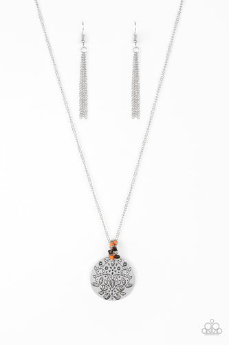 A floral embossed silver disc and dainty wooden and orange stone beads swing from the bottom of a lengthened silver chain for a whimsical look. Features an adjustable clasp closure.
