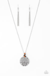 A floral embossed silver disc and dainty wooden and orange stone beads swing from the bottom of a lengthened silver chain for a whimsical look. Features an adjustable clasp closure.