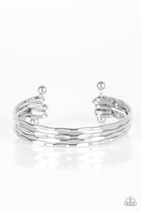 Delicately hammered in sections of shimmer, glistening silver bars are threaded along two metallic rods, creating a layered cuff across the wrist.