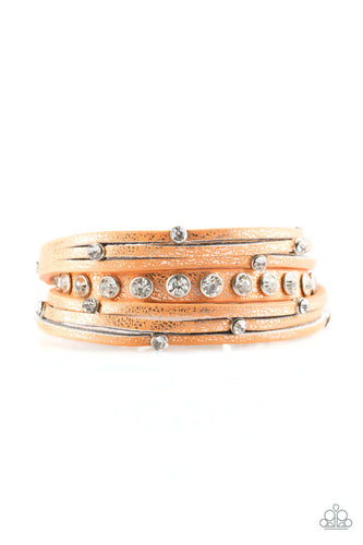 Dusted in a golden shimmer, a skinny strip of orange leather is spliced into sections of glittery strands. Infused with white rhinestones, the elongated band double wraps around the wrist for a fierce one-of-a-kind look. Features an adjustable snap closure.  Sold as one individual bracelet.