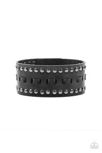 Black laces are threaded through the center of a black leather band that has been studded in gunmetal accents, creating a rustic centerpiece around the wrist. Features an adjustable snap closure.  Sold as one individual bracelet.