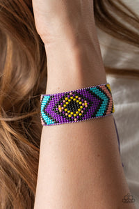 A dainty collection of purple, yellow, black, Rose Tan, and blue beads are delicately weaved into a colorful textile pattern across the wrist for a southwestern inspired fashion. Features an adjustable sliding knot closure.