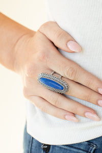 An oblong blue stone adorns the center of an elongated silver frame featuring mismatched silver textures for a bold artisan look. Features a stretchy band for a flexible fit.