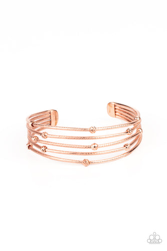 Ornate shiny copper beads are haphazardly threaded along textured shiny copper bars that layer across the wrist, coalescing into an airy cuff.