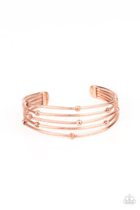 Ornate shiny copper beads are haphazardly threaded along textured shiny copper bars that layer across the wrist, coalescing into an airy cuff.