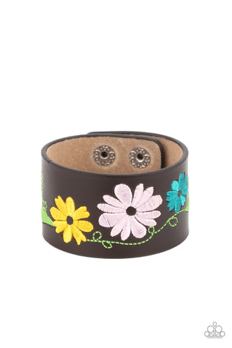A colorful floral pattern is embroidered across the front of a brown leather band, creating a whimsical centerpiece around the wrist. Features an adjustable snap closure.