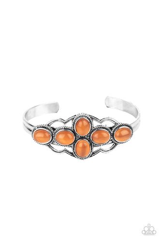 A collection of glowing orange cat's eye stones delicately cluster inside a scalloped silver frame, creating an ethereal centerpiece atop a dainty silver cuff.