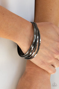 A set of four plain gunmetal bangles interlocks with four glistening gunmetal bangles etched in a tread-like pattern, creating an edgy stacked look around the wrist