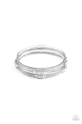 Pairs of plain, textured, and white rhinestone adorned silver bangles glide along the wrist for a sparkly look