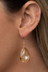 A golden rhinestone gem is threaded along a rod inside a gold teardrop casing, creating a glamorous lure. Earring attaches to a standard fishhook fitting.