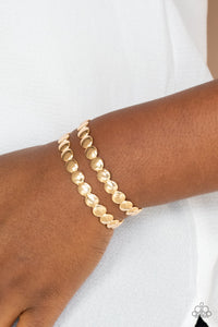 Brushed in a shiny finish, rows of flattened gold studs coalesce into a shimmery cuff around the wrist.