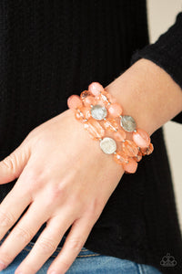 Glassy and opaque coral crystal-like beads and textured silver accents are threaded along stretchy bands around the wrist, creating mystical layers