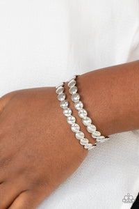 Brushed in a shiny finish, rows of flattened silver studs coalesce into a shimmery cuff around the wrist.