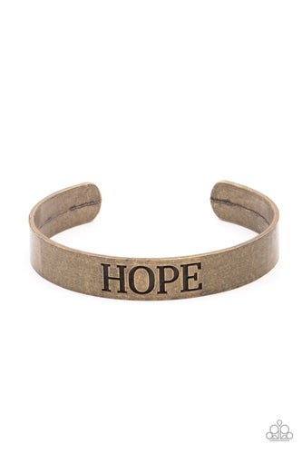 The center of a rustic brass cuff is stamped in the word, 