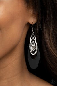 Infused with a glassy white rhinestone, shiny silver ovals, a twisted silver plate, and an oversized black frame trickle along a shimmery silver chain, creating a noise-making tassel. Earring attaches to a standard fishhook fitting. 