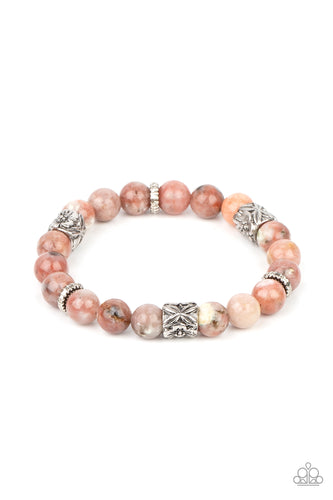 An earthy collection of natural pink stone beads, textured silver rings, and floral embossed beads are threaded along stretchy bands around the wrist, creating a seasonal centerpiece. 