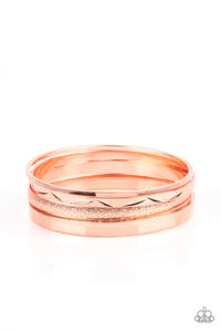 Varying in hammered, textured, and high sheen finishes, a mismatched collection of shiny copper bangles stacks across the wrist for a classic fashion. 