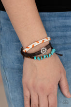 Load image into Gallery viewer, Featuring a silver floral centerpiece, mismatched strands of  turquoise stones and wooden beads, brown leather, and braided orange and white cording layers across the wrist for a seasonal flair. Features an adjustable sliding knot closure. 
