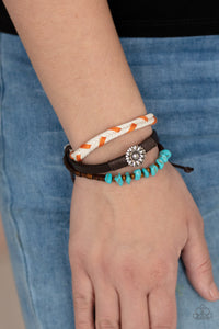 Featuring a silver floral centerpiece, mismatched strands of  turquoise stones and wooden beads, brown leather, and braided orange and white cording layers across the wrist for a seasonal flair. Features an adjustable sliding knot closure. 