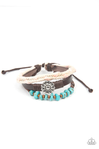 Featuring a silver floral centerpiece, mismatched strands of turquoise stones and wooden beads, brown leather, and braided pink and white cording layers across the wrist for a seasonal flair. Features an adjustable sliding knot closure.
