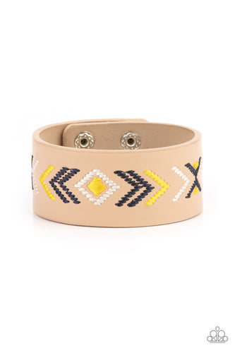 Yellow, blue, and white thread is stitched across the front of a brown leather band, creating a colorful tribal inspired pattern. Features an adjustable snap closure.