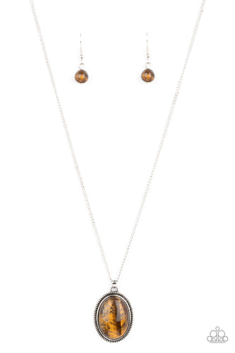 An oval tiger's eye stone is pressed into the center of a studded silver frame, creating a tranquil pendant below the collar. Features an adjustable clasp closure.