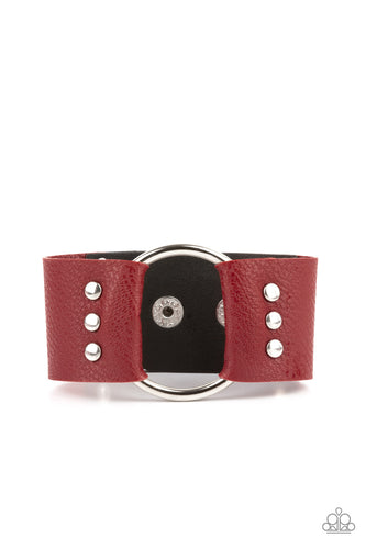 An oversized silver hoop is studded in place between the center of studded pieces of red and black leather, creating a rustic centerpiece around the wrist. Features an adjustable snap closure. 