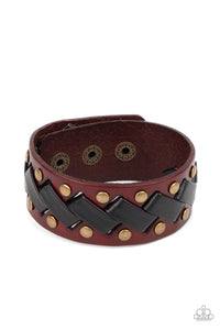 Thick black leather laces zigzag across the front brass studded brown leather band, creating a rustic display around the wrist. Features an adjustable snap closure.