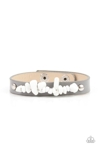 A strand of white pebbles is studded in place across the front of a skinny gray leather band, creating a colorful earthy display around the wrist. Features an adjustable snap closure.