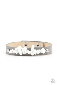 A strand of white pebbles is studded in place across the front of a skinny gray leather band, creating a colorful earthy display around the wrist. Features an adjustable snap closure.