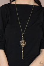 Load image into Gallery viewer, Infused with brass beaded accents, a lifelike brass palm leaf frame attaches to the bottom of a rustic brass chain. An antiqued brass chain tassel swings from the bottom, adding flirtatious movement to the summery statement piece. Features an adjustable clasp closure. 
