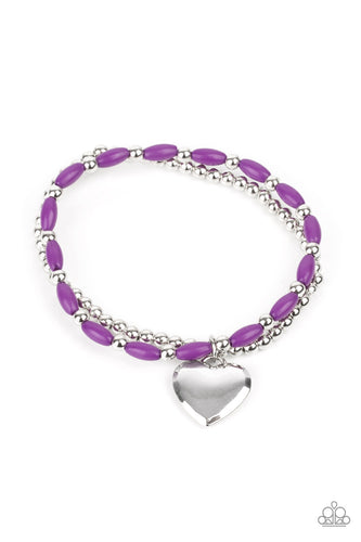 A shiny silver heart dangles from a strand of playful purple beads. It is paired with a strand of round silver beads threaded along a stretchy band for a whimsical charm around the wrist
