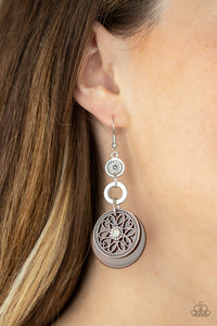 Reminiscent of an eclipse, an airy silver ring radiating with ornate petals, sways in front of a brown shell-like disc. Silver rings in graduating sizes cascade from the top for a whimsically nautical look. Earring attaches to a standard fishhook fitting.