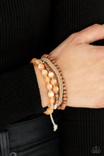 Load image into Gallery viewer, Strands of glassy orange cat&#39;s eye beads stand out in an earthy collection of wooden beads and braided twine, giving a polished flair to the natural homespun look as it stacks up the wrist. Features an adjustable sliding knot closure. 
