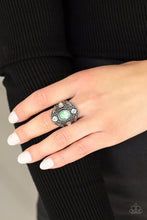 Load image into Gallery viewer, A dewy green gem adorns the center of an oversized antiqued frame embossed in silver leafy vine-like filigree. Round and teardrop white rhinestones adorn the four points of the frame, adding a classic sparkle to the ethereal centerpiece. Features a stretchy band for a flexible fit.
