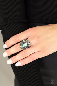 A dewy green gem adorns the center of an oversized antiqued frame embossed in silver leafy vine-like filigree. Round and teardrop white rhinestones adorn the four points of the frame, adding a classic sparkle to the ethereal centerpiece. Features a stretchy band for a flexible fit.