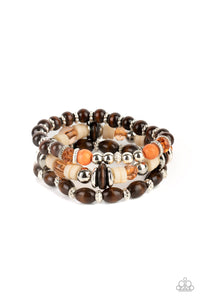 A mismatched collection of brown wooden beads, silver accents, orange stones, Buttercream discs, and glassy Desert Mist beads are threaded along stretchy bands, creating colorful layers around the wrist. 