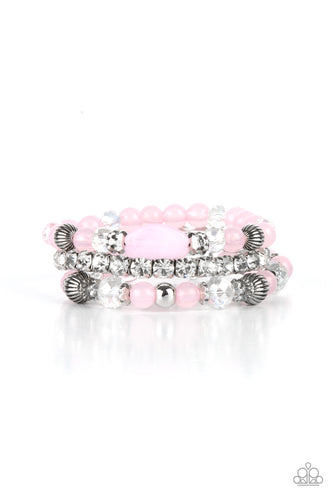 Infused with a stretchy strand of glassy white rhinestones, a mismatched collection of cloudy pink, white crystal-like, and ornate silver accents are threaded along stretchy bands around the wrist, creating ethereal layers. 