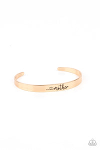 A dainty gold cuff is stamped in a heart and the word, "Mother," creating a sentimental centerpiece around the wrist