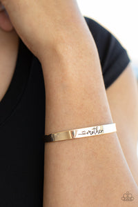 A dainty gold cuff is stamped in a heart and the word, "Mother," creating a sentimental centerpiece around the wrist