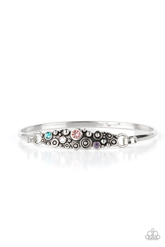 A cluster of engraved and antiqued silver swirls merge with colorful rhinestones and coalesce into a whimsical display across the wrist on a dainty silver cuff. Features a hook and eye closure. 