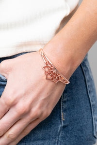 Brushed in a high sheen finish, an airy mandala-like frame crowns the top of a dainty shiny copper cuff for a whimsically seasonal flair.