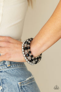 Sections of shiny silver beads and an alternating pattern of smoky and glittery black rhinestone gems gradually increase in size along a coiled wire, creating a jaw-dropping infinity wrap bracelet around the wrist.