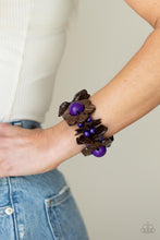 Load image into Gallery viewer, Distressed brown wooden pieces and round purple wooden beads join colorful wooden floral accents along stretchy bands around the wrist, creating a tropical inspired centerpiece. 
